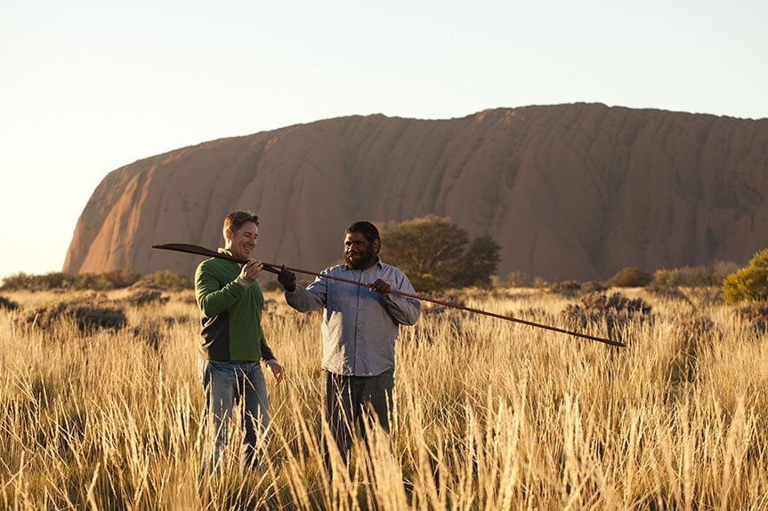 an indigenous man showing a tourist an atlatl