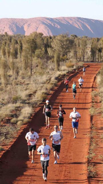 Runners compete in the Australian Outback Marathon with Uluru in the background